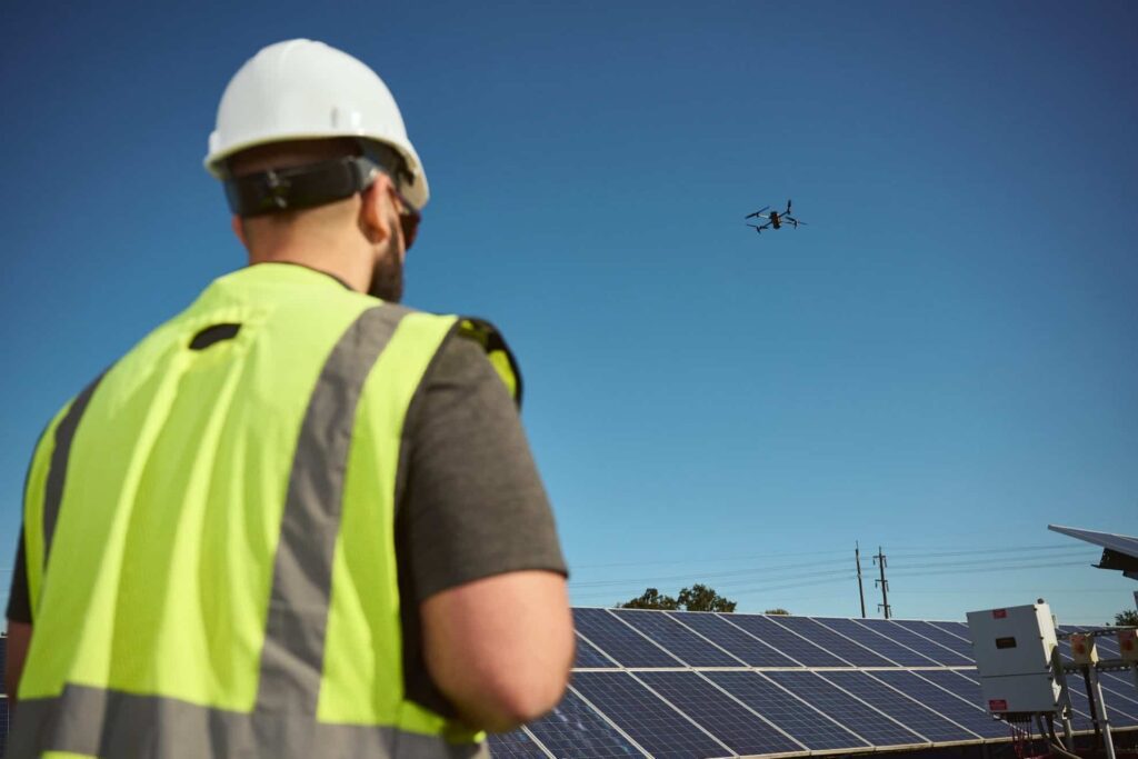 Man in yellow vest flying drone over solar panels 